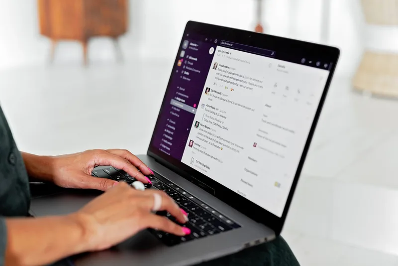 A woman typing a message on a laptop in a modern office, representing outreach to community forums and professional networks for survey distribution