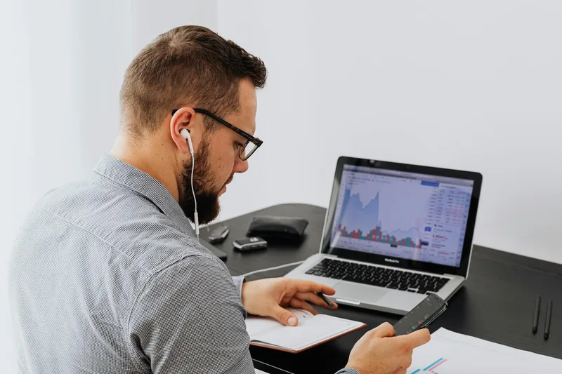 Person researching market demand on a laptop with a notebook beside them