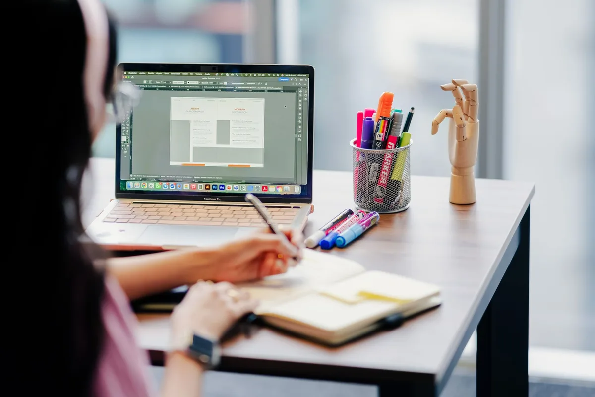 A designer sketching ideas on a notepad next to a laptop in a modern office