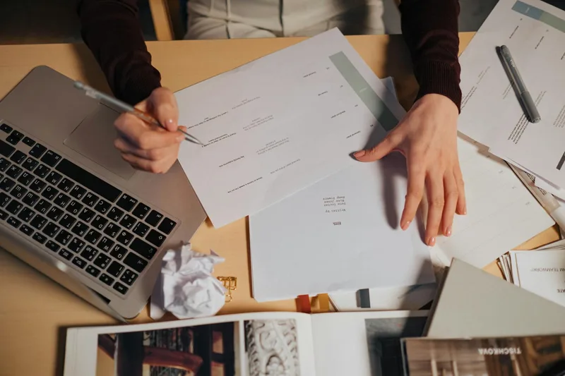 A person reviewing a handwritten notepad and laptop screen after a research session, organizing findings