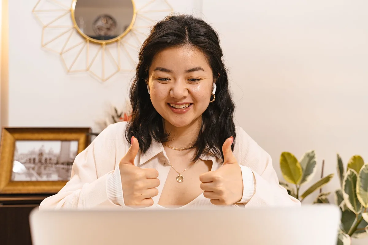 A solopreneur at a laptop, looking encouraged by a conversation about their idea, with a notebook open showing enthusiastic checkmarks next to “would you pay?” responses that do not match actual sales numbers